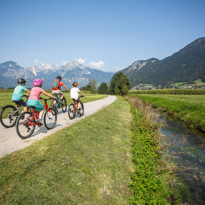 Familie mit Kindern fährt auf dem Radweg am Ziller entlang im Sommer durch das Zillertal